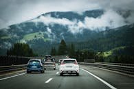 A scenic drive on a mountain road in Austria, surrounded by lush forests and clouds.